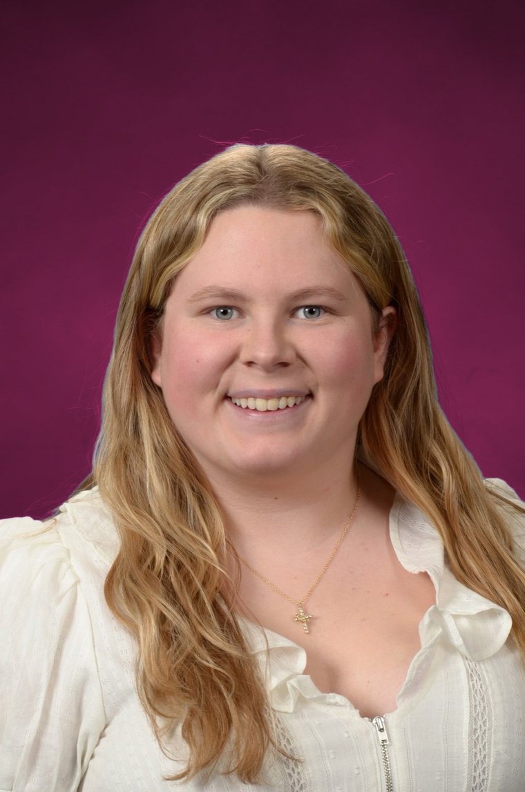 Sara Barkouras smiling, with long blonde hair, a white ruffled blouse, and a small gold cross necklace.